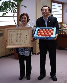 表彰状を持つ佐藤イネ子さんと佐藤さんが作ったトマトを持つ三村知事